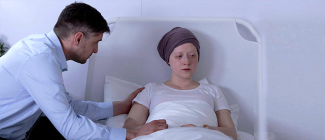man conforting wife in hospital bed undergoing chemotherapy
